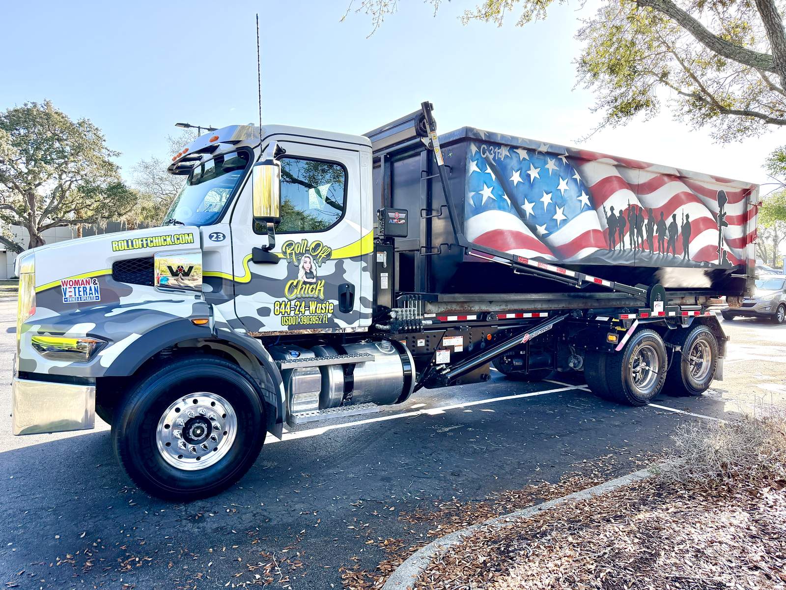 Roll-off truck with a blue flag-painted container parked in a yard