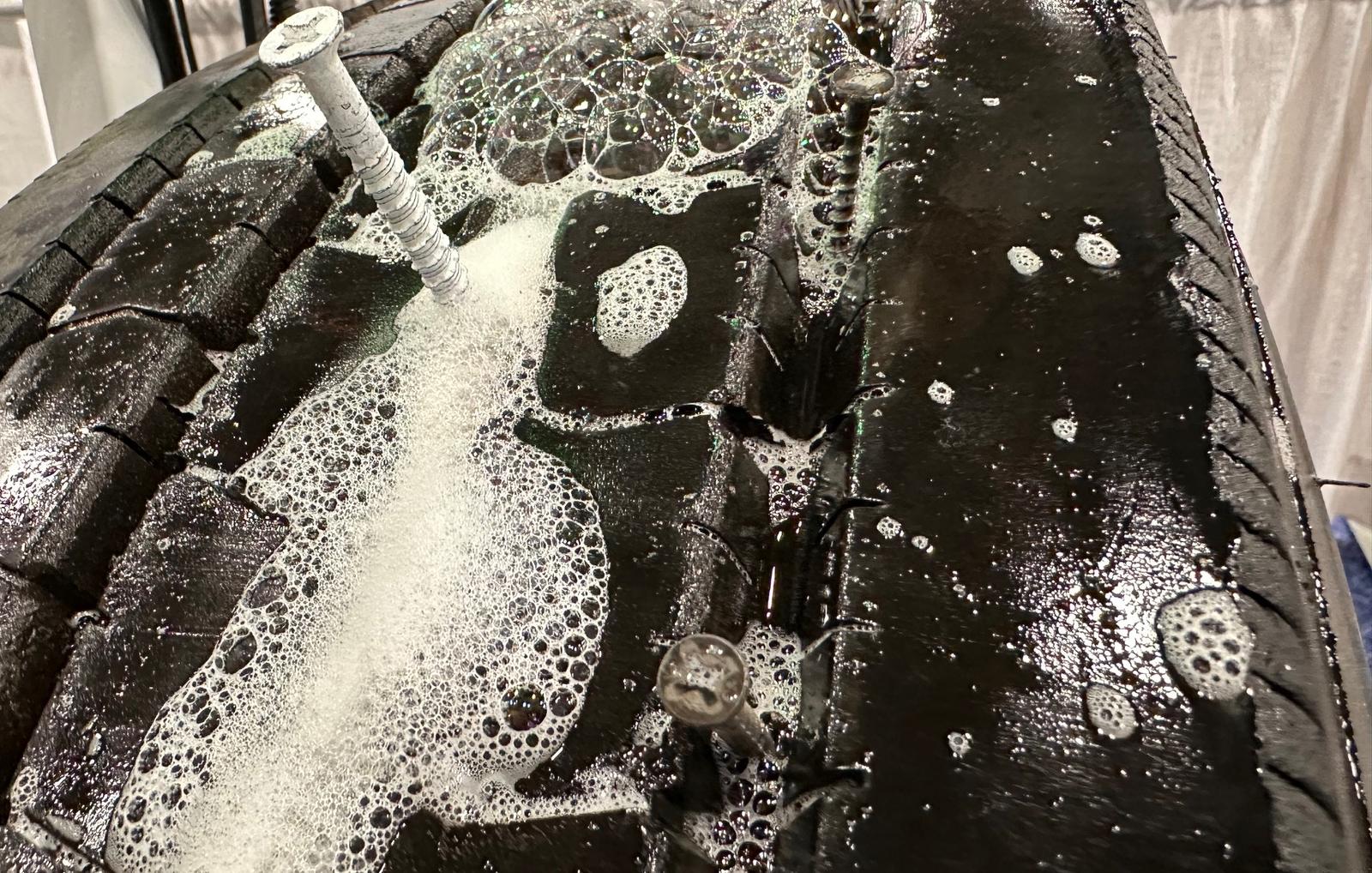 Screws driven into a truck tire tread with soapy water bubbling at the punctures